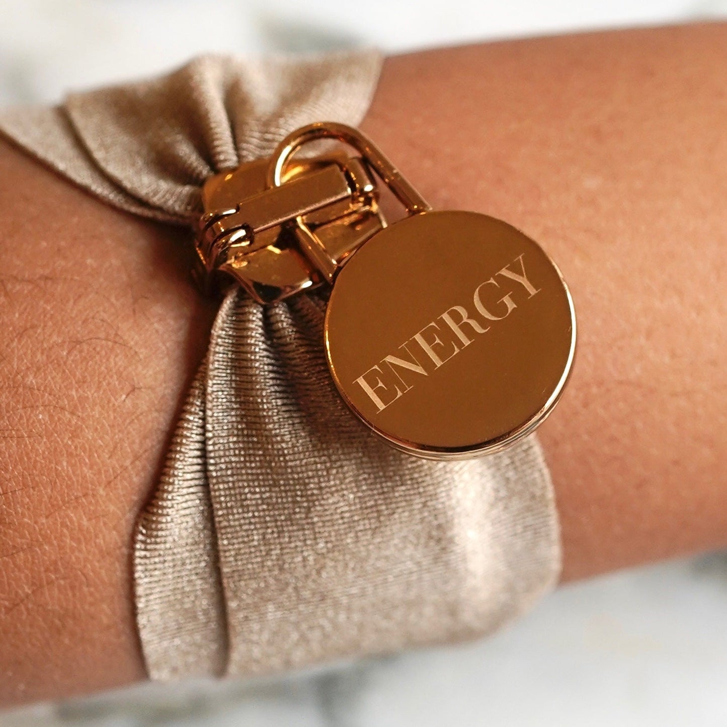 Close-up of a coffee-colored energy bracelet with a gold charm engraved with the word "ENERGY" from the Nourish Your Energy Duo.