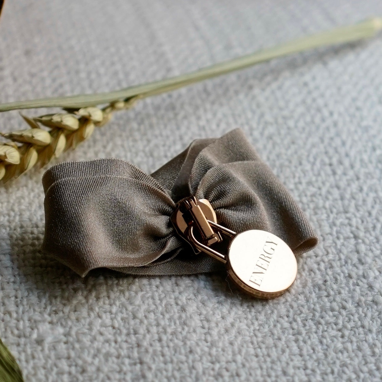 Engraved energy bracelet with brown fabric band and rose gold clasp on grey surface