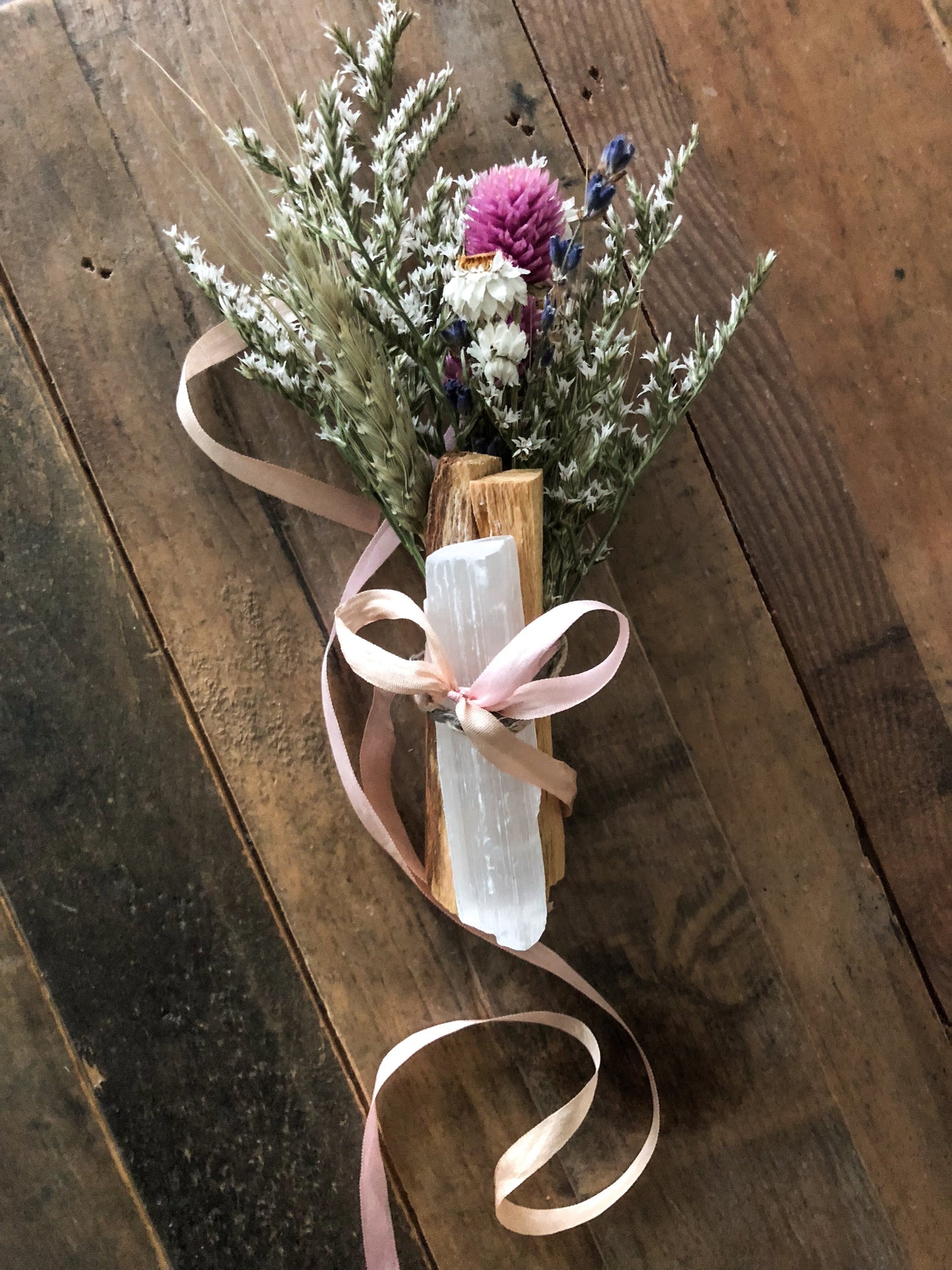 Uplifting Palo Santo Selenite floral bouquet with pink, white, and yellow dried flowers and tied with a pink ribbon on wooden background