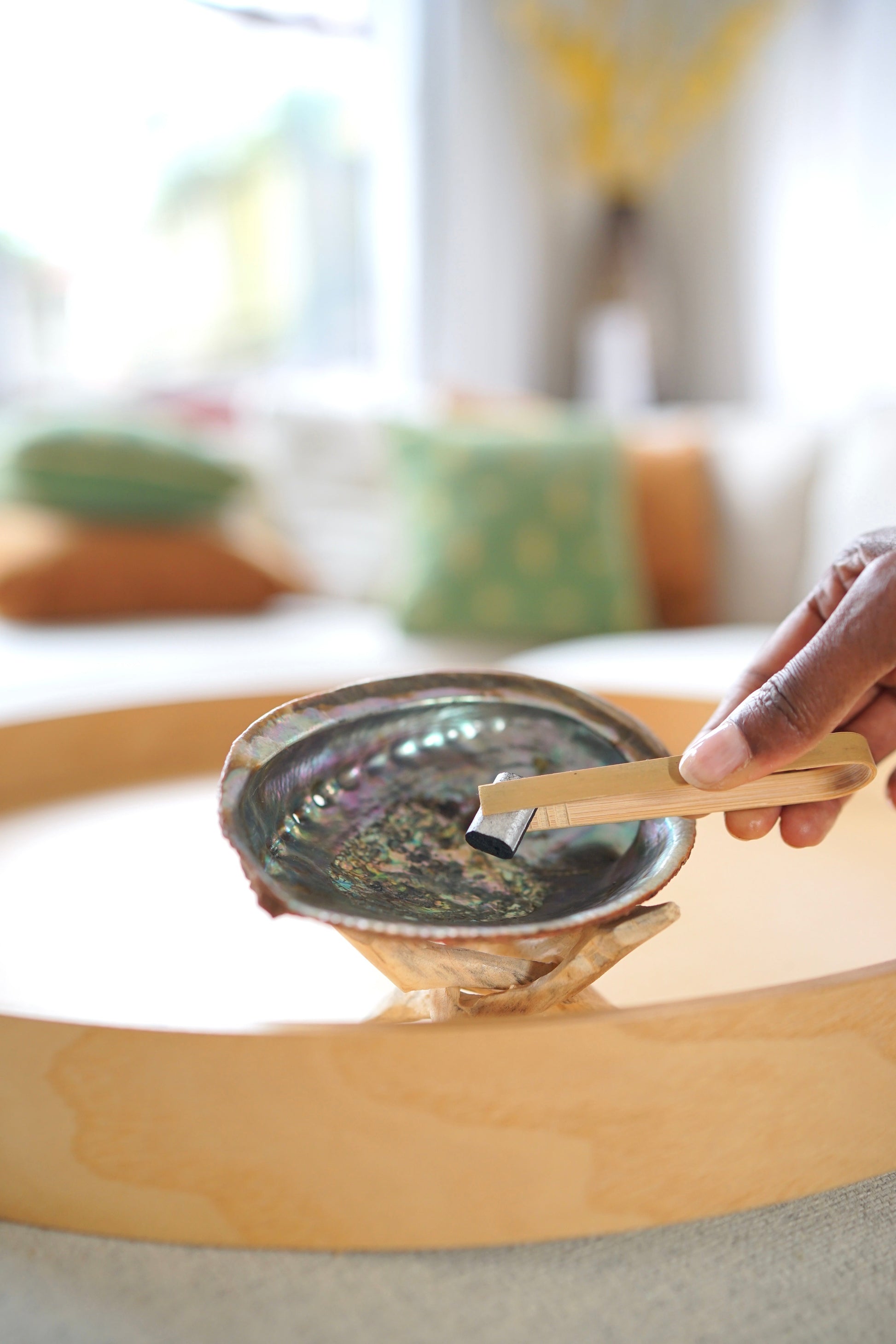 Hand holding New Beginnings Herbal Incense charcoal over abalone shell burner in cozy living room setting
